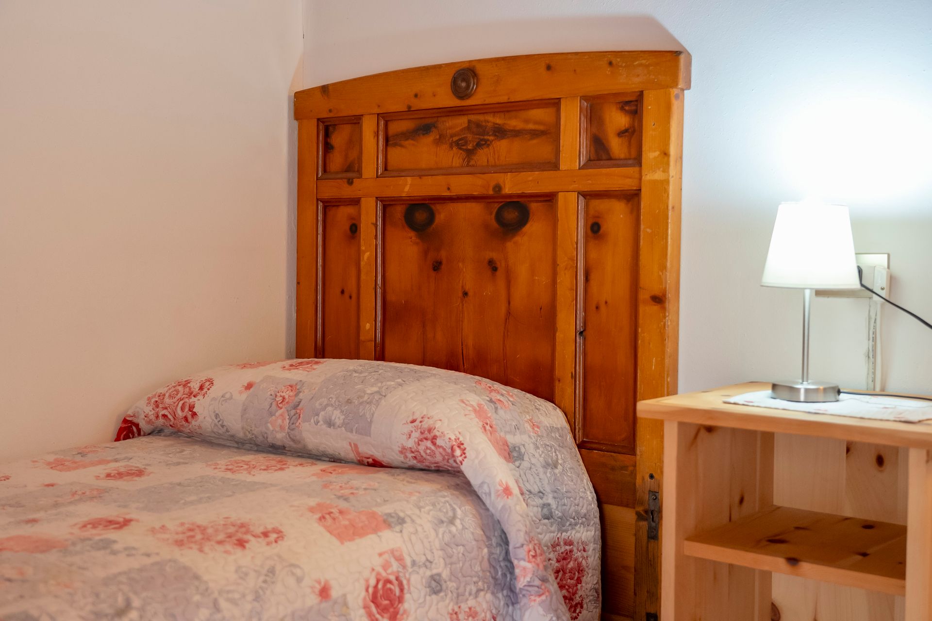 Una camera da letto con letto, comodino, lampada e testiera in legno.