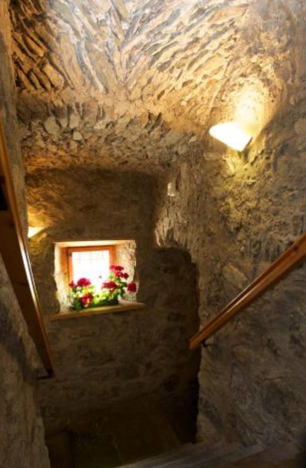 Una scala in pietra con una ringhiera in legno e una finestra con dei fiori.