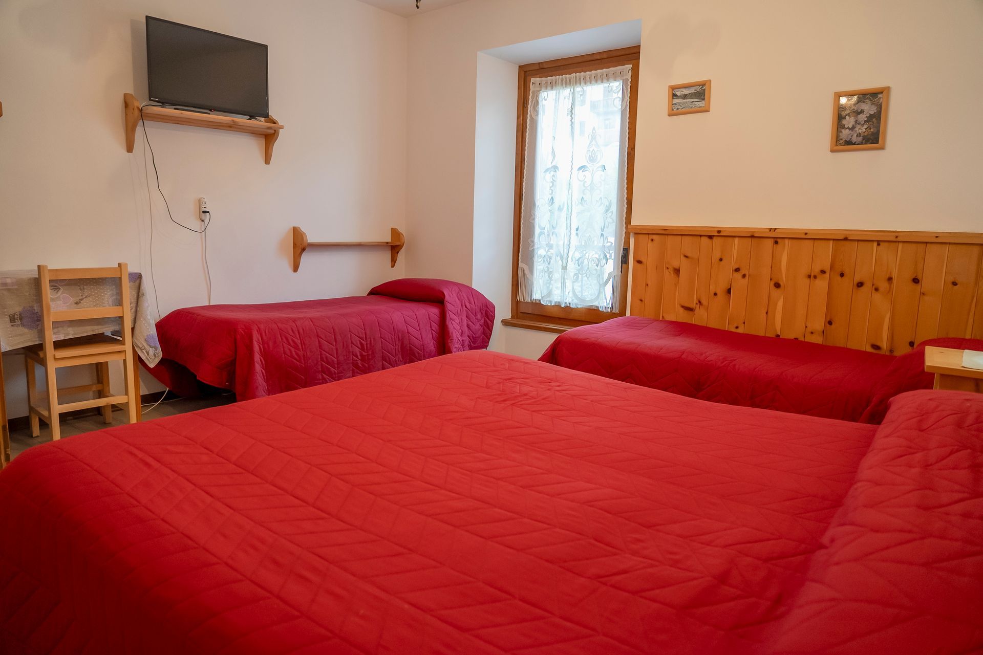 Una camera d'albergo con tre letti e una tv a schermo piatto.