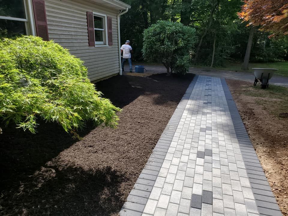 A man is standing in front of a house next to a brick walkway.