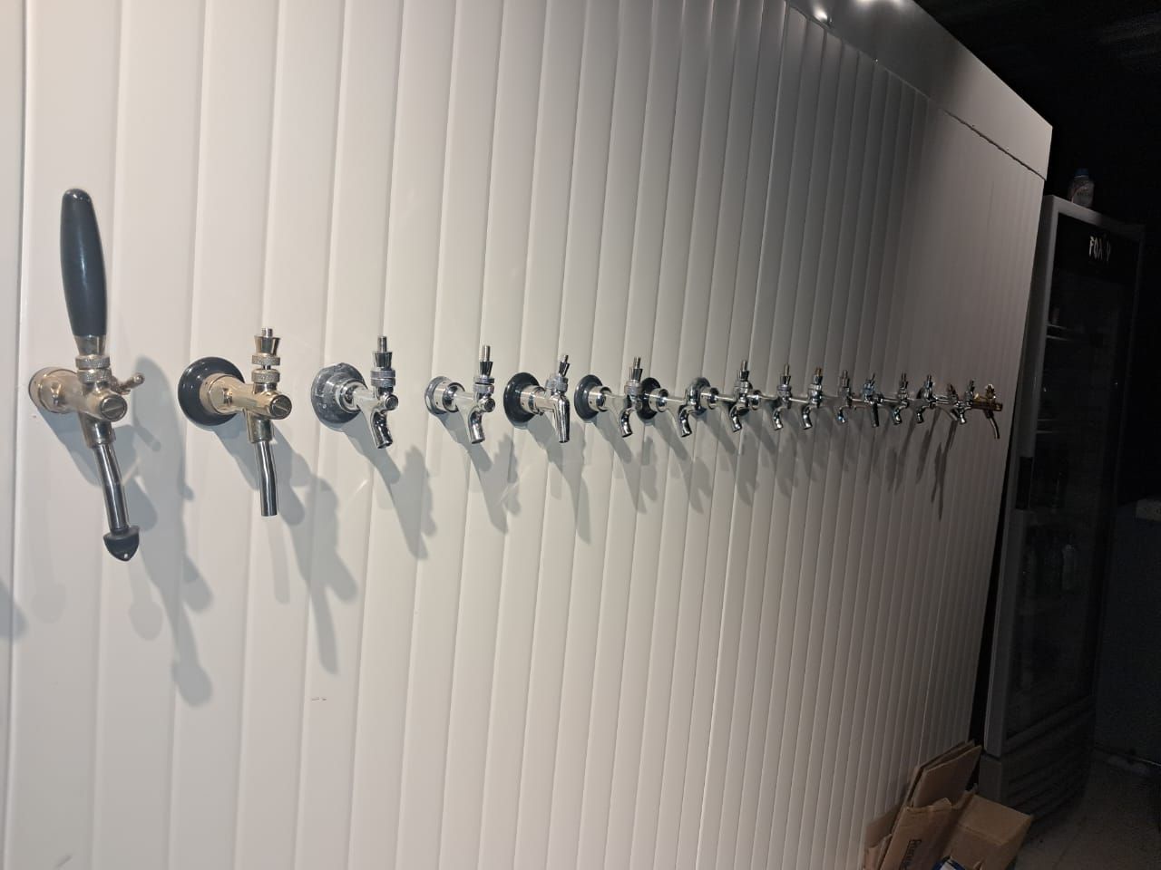 Fila de grifos de cerveza montados en una pared blanca texturizada.
