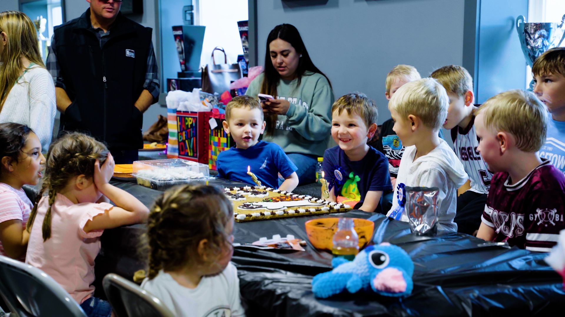 A group of children are sitting around a table at a birthday party.