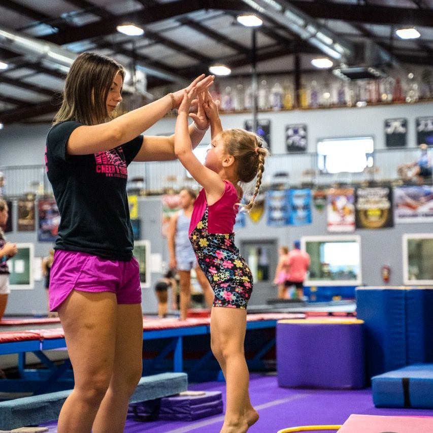 A woman is helping a little girl do a handstand in a gym.