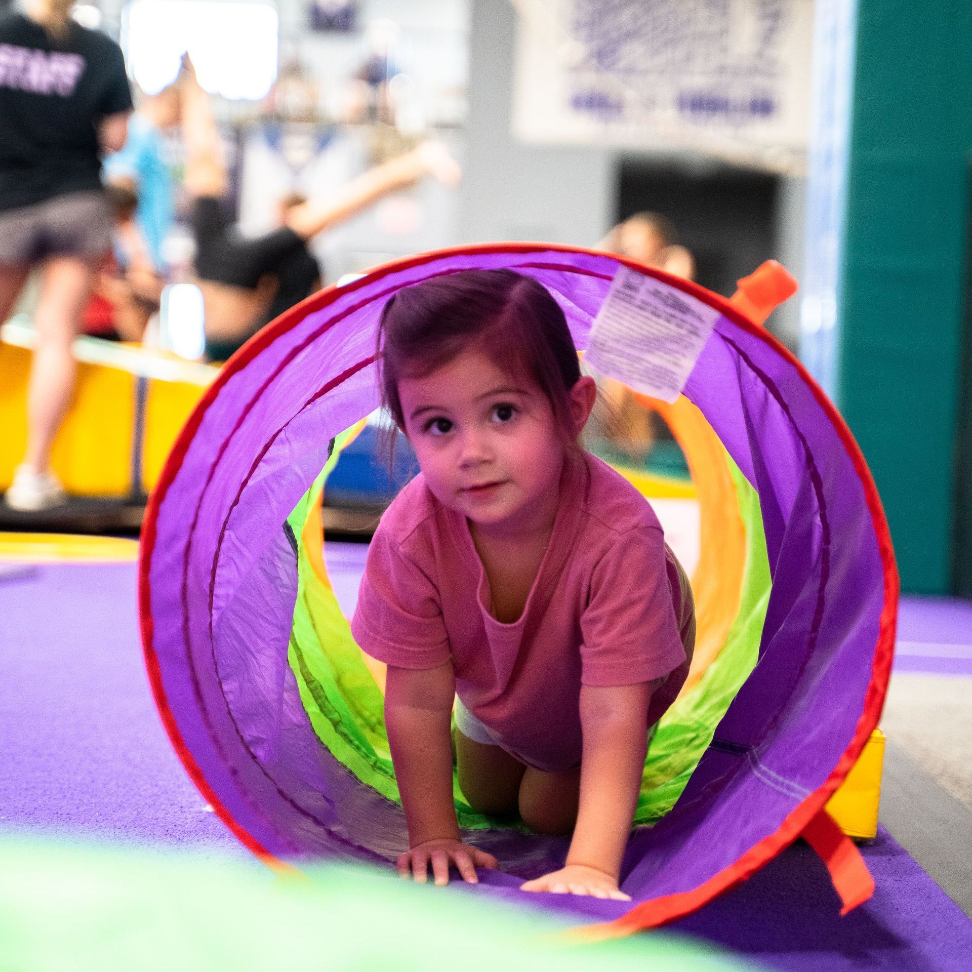 A little girl is crawling through a purple tunnel