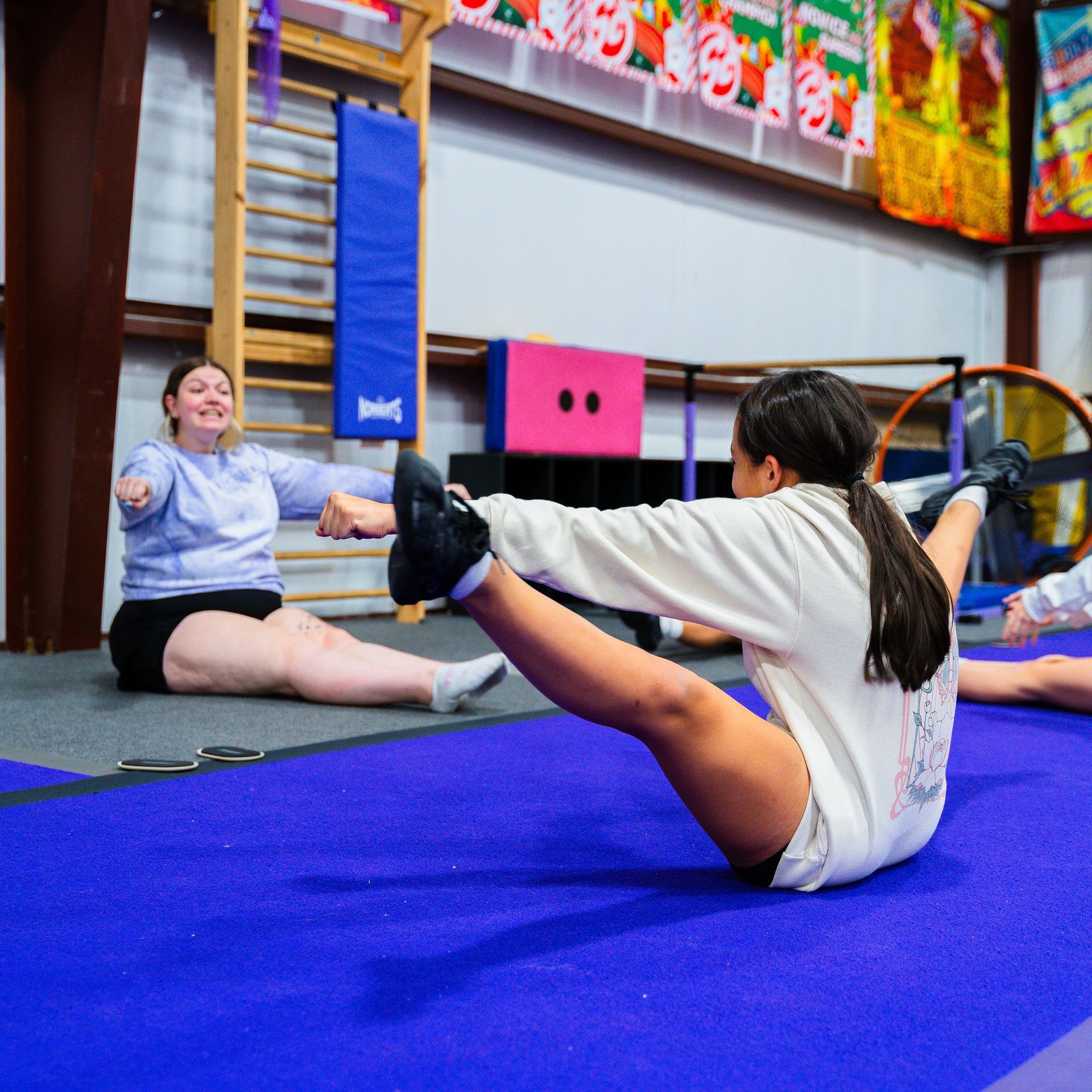 A group of people are doing exercises on a blue mat in a gym.