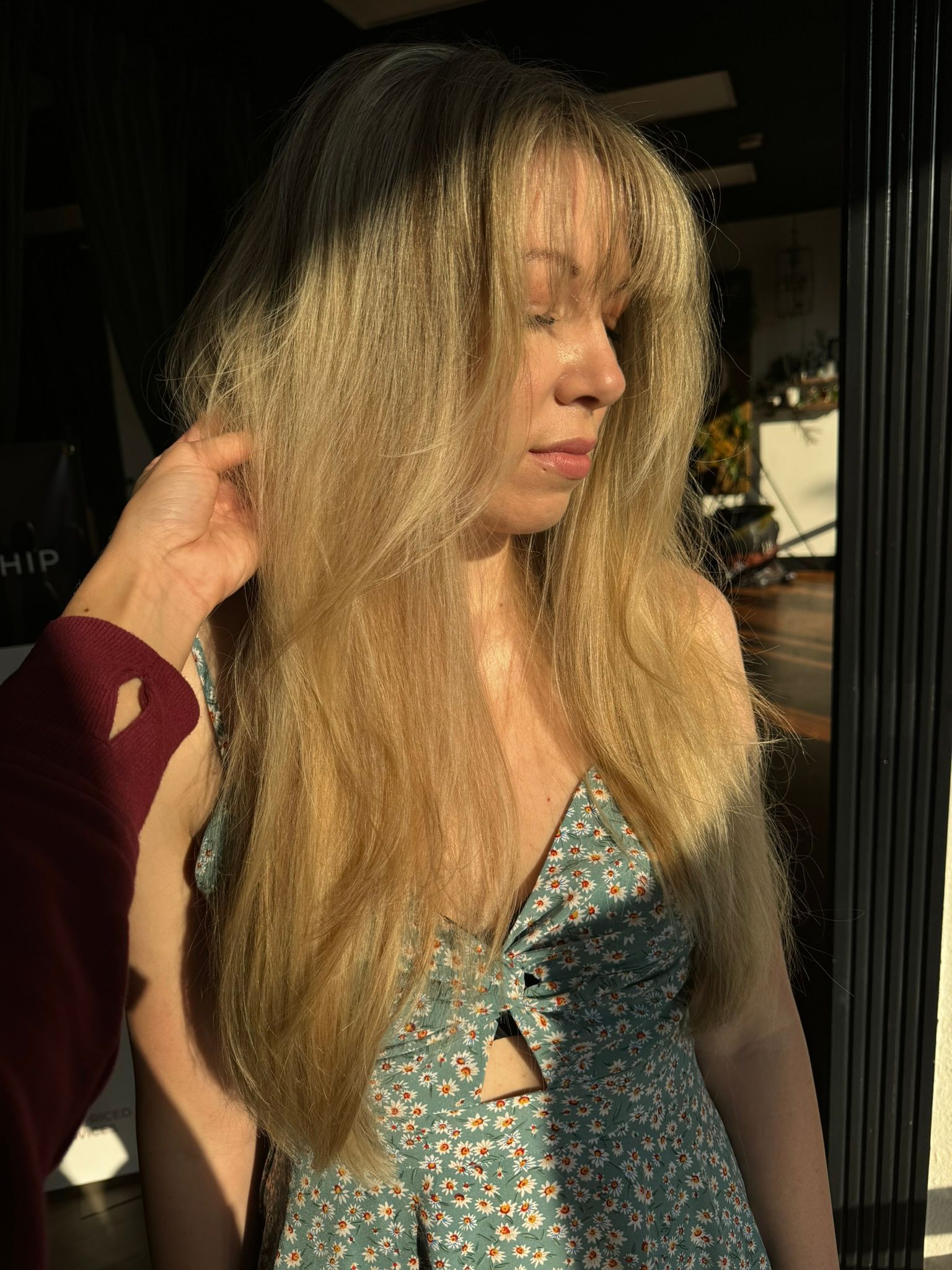 A woman with long blonde hair is standing in front of a window