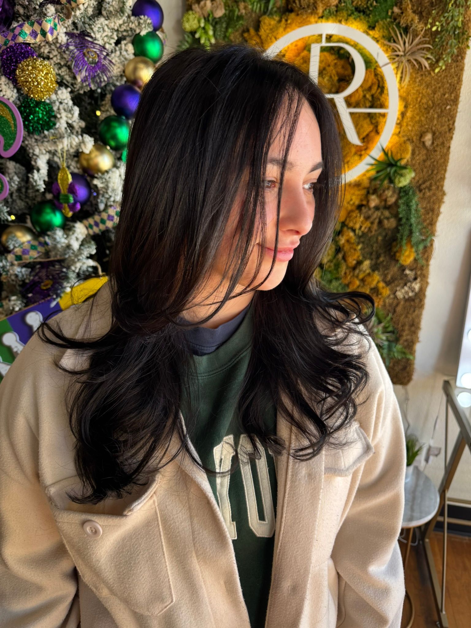A woman with long black hair is standing in front of a christmas tree