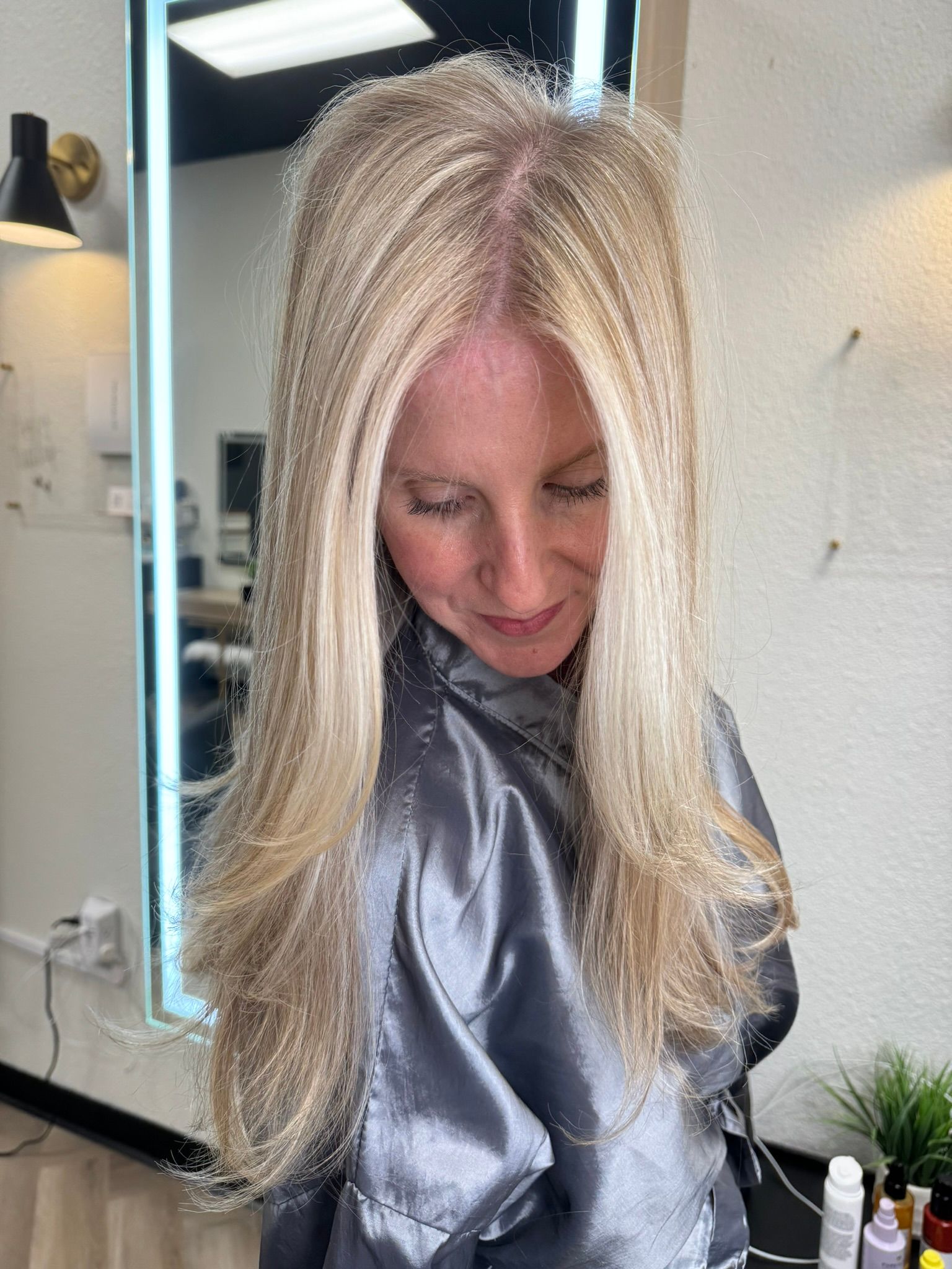 A woman with blonde hair is standing in front of a mirror in a salon