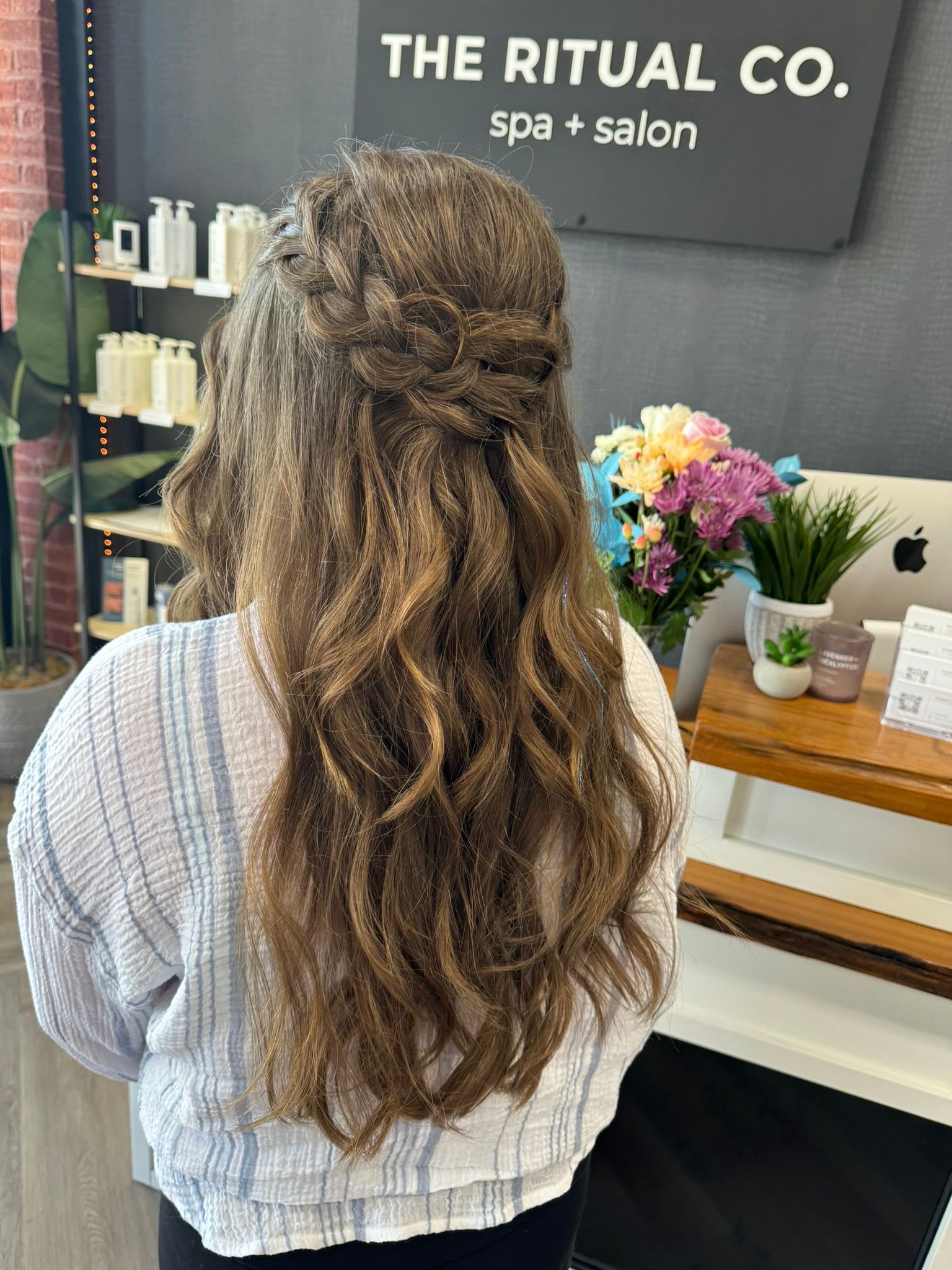 A woman with long hair is standing in front of a sign that says the ritual co. spa salon