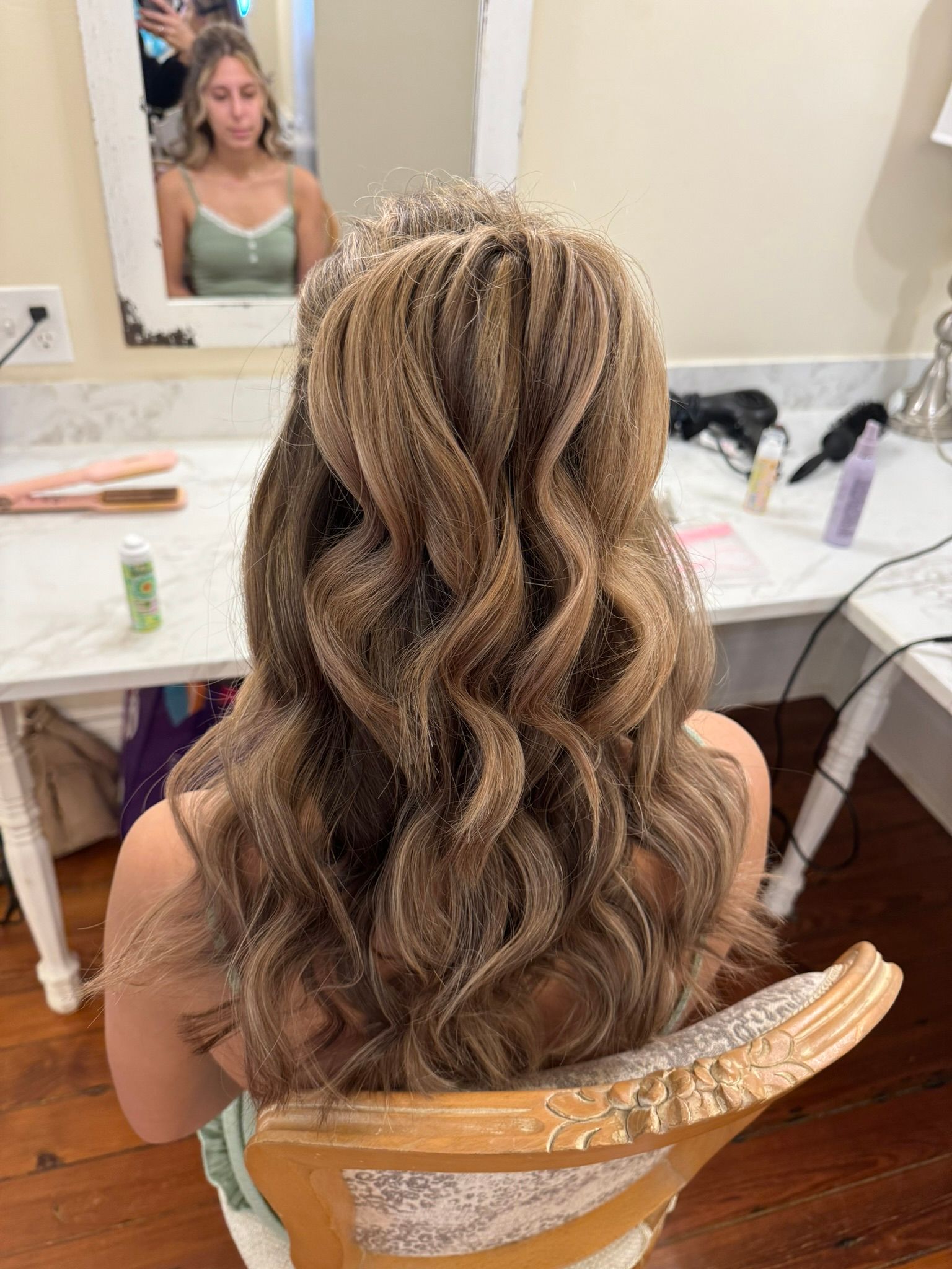 A woman is sitting in a chair with her hair in a half up half down hairstyle
