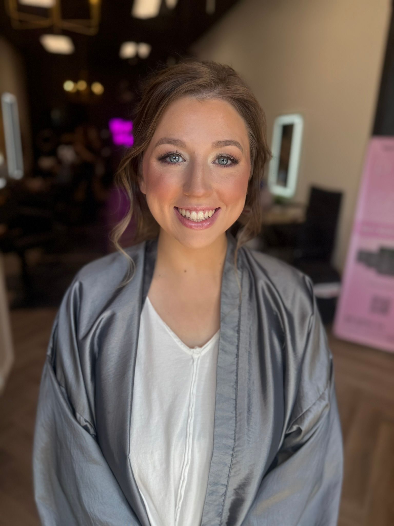 A woman is wearing a gray robe and smiling in a salon