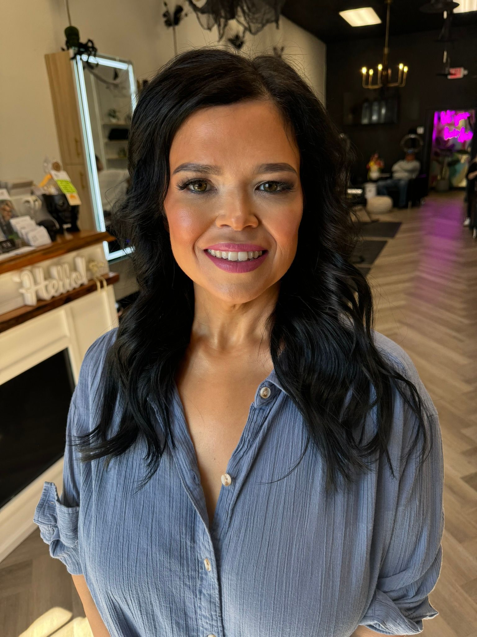 A woman in a blue shirt is smiling in a salon