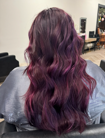 A woman with long purple hair is sitting in a chair in a salon