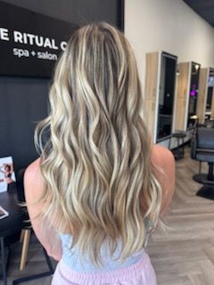 Woman with long, wavy blonde hair; standing in a salon.