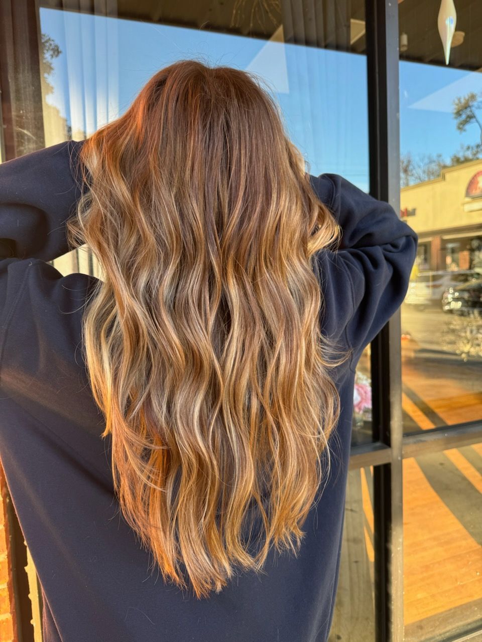 A woman with long brown hair is standing in front of a window