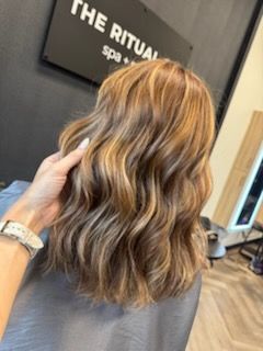 Woman's wavy, highlighted brown hair styled at a salon. A hand touches the hair. 
