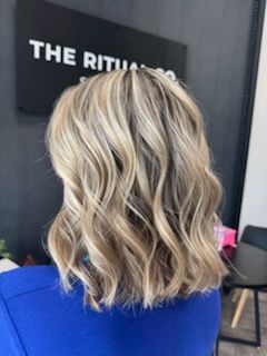 Blonde, wavy bob hairstyle with highlights, viewed from the back. In a salon setting.