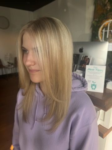Blonde woman with layered haircut, wearing a purple hoodie. Inside a salon.