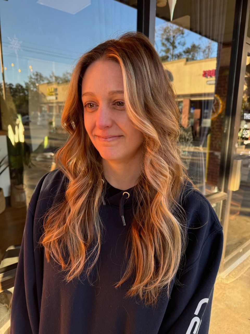 A woman with long brown hair is wearing a black sweatshirt and smiling