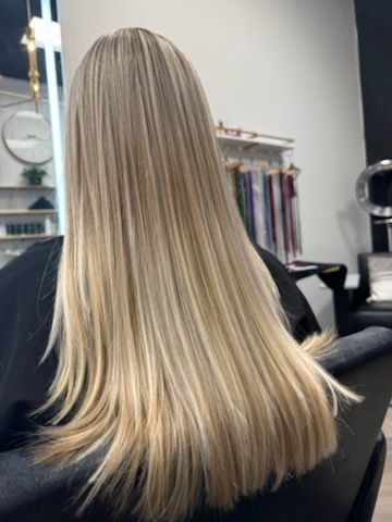 Woman with long, straight blonde hair with highlights, sitting in a salon chair.
