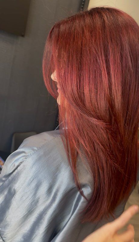 Woman with long, layered red hair, smiling. Wearing a blue silky robe, indoors.
