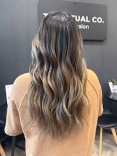 Woman with long, wavy, highlighted hair, standing in a salon.