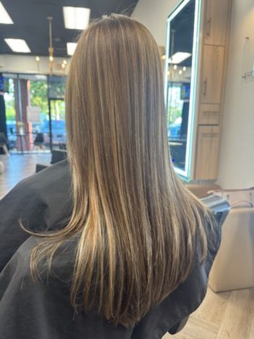 Woman with long, straight, highlighted brown hair in a salon.