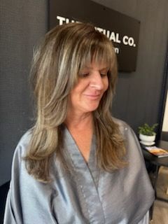 Woman with layered blonde hair and bangs, wearing a gray robe.