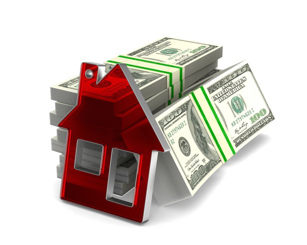 A single-story, beige brick house with a dark roof and a covered porch, set on a grassy lot shaded by a large oak tree.