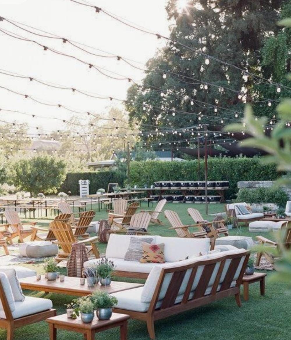 Reunión al aire libre con luces de cadena, áreas para sentarse y un exuberante césped verde.
