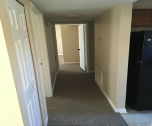 A hallway with a black refrigerator in the corner
