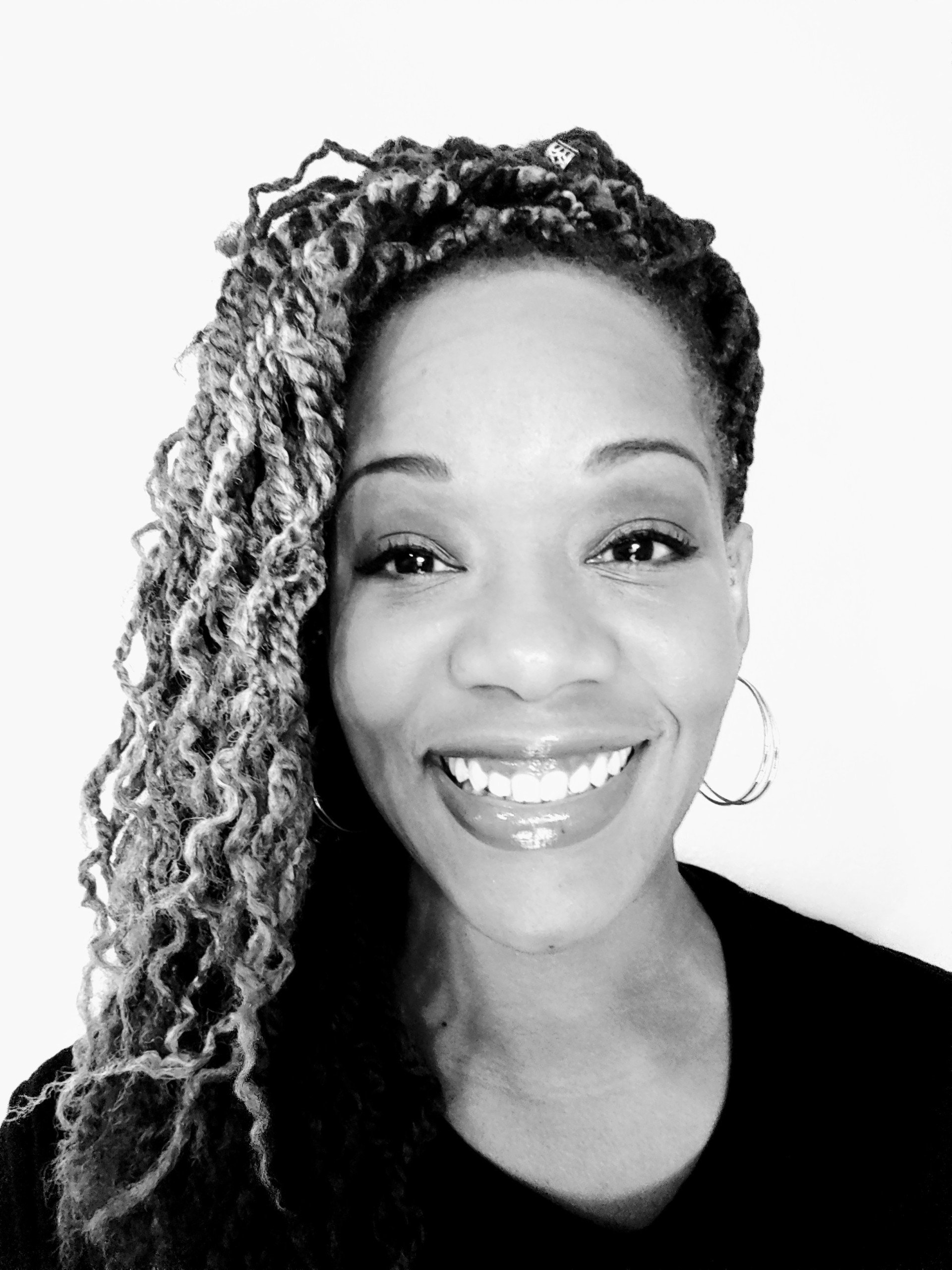A woman with dreadlocks is smiling in a black and white photo.
