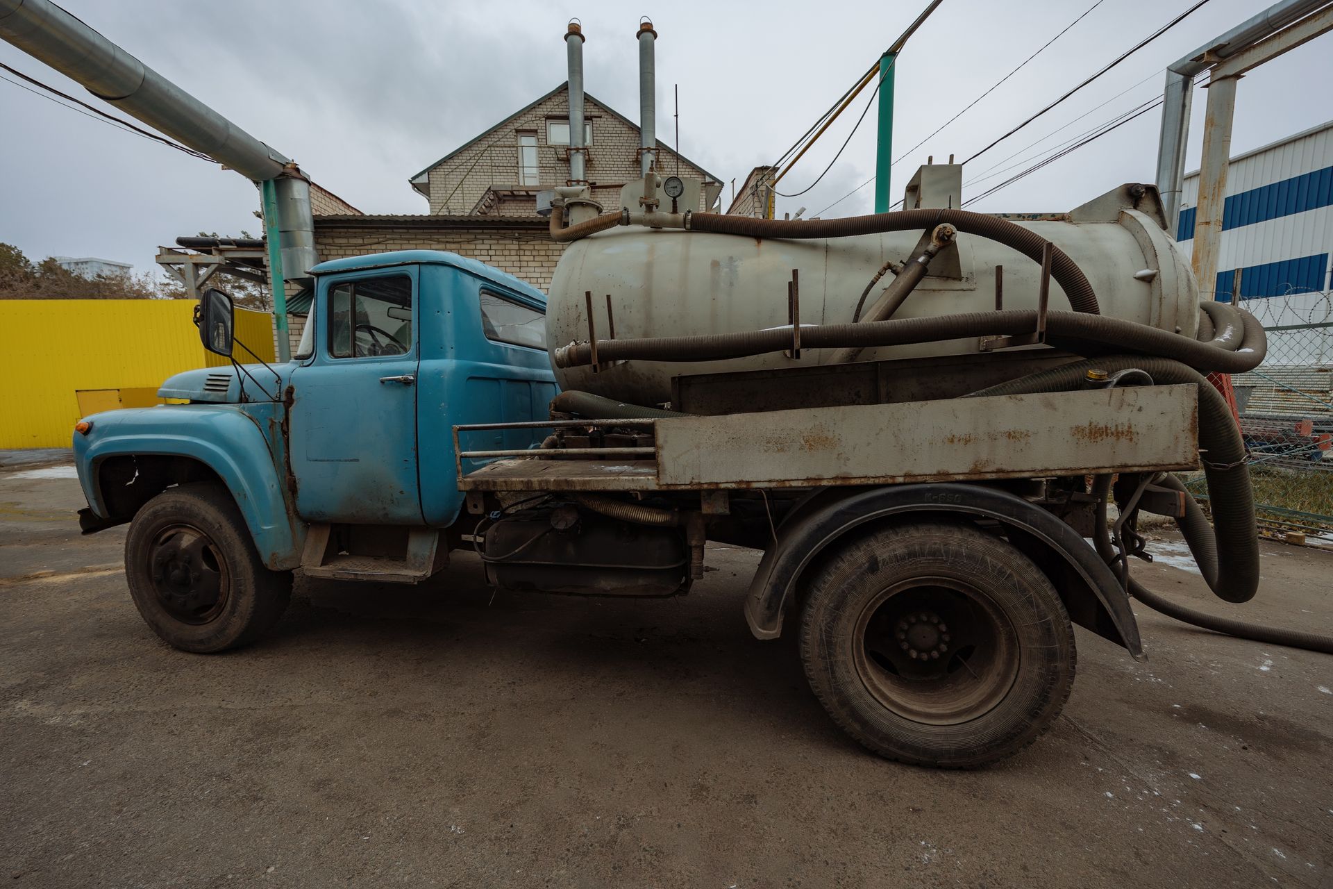 Blue septic truck parked in front of a building, with a cloudy sky in the background.