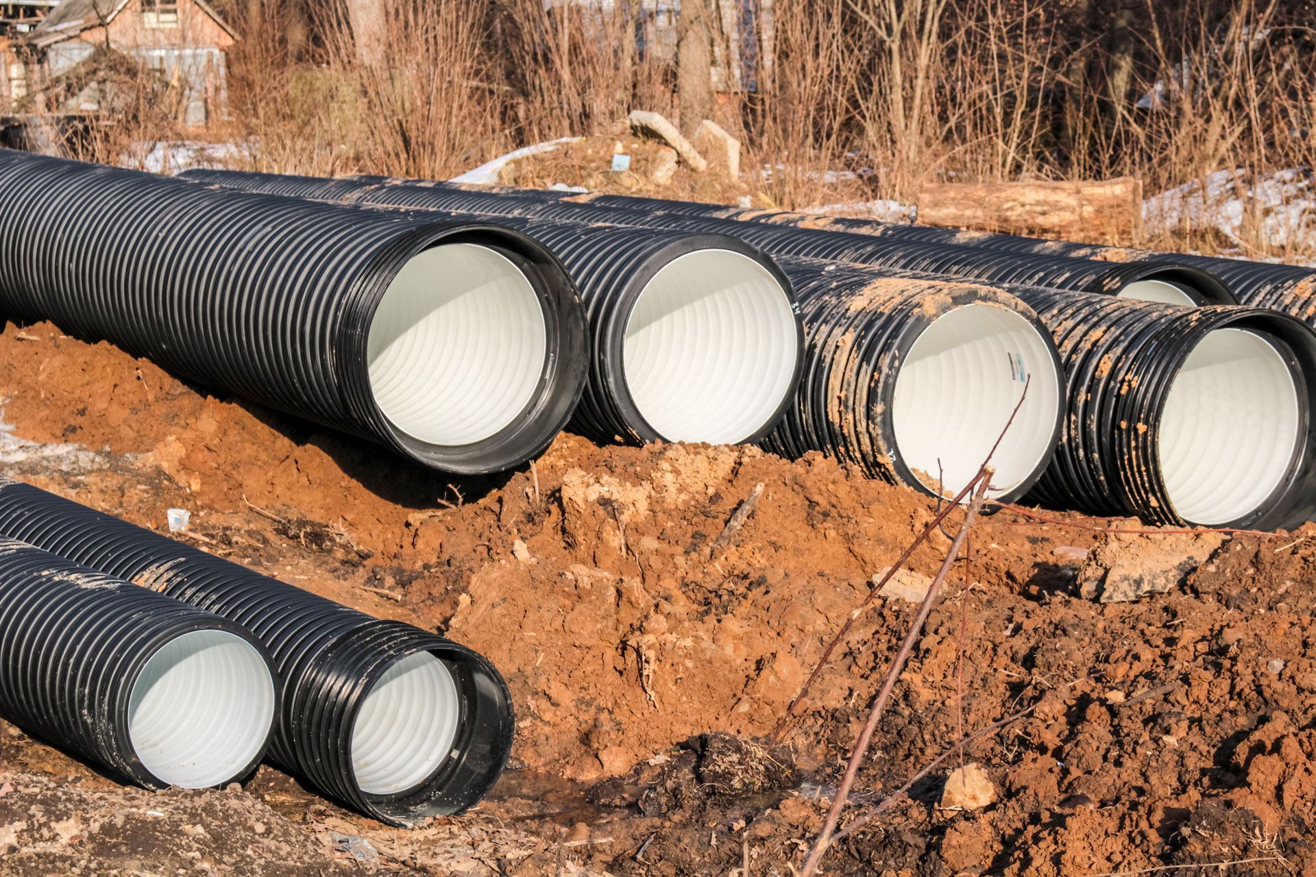 Black corrugated drainage pipes laid in a dirt trench, ready for installation.