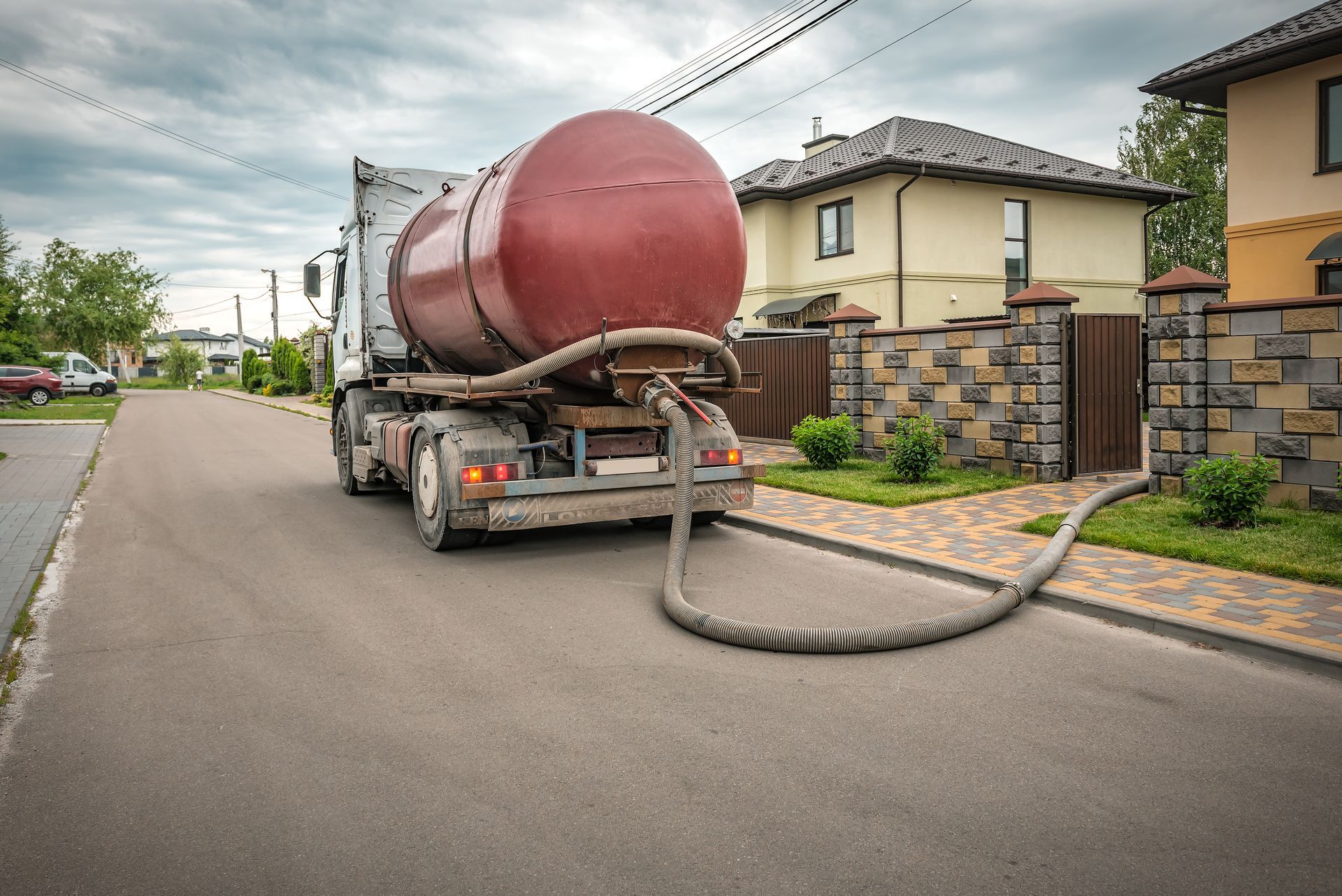Tanker truck parked on residential street, hose connected to a house for fuel delivery.