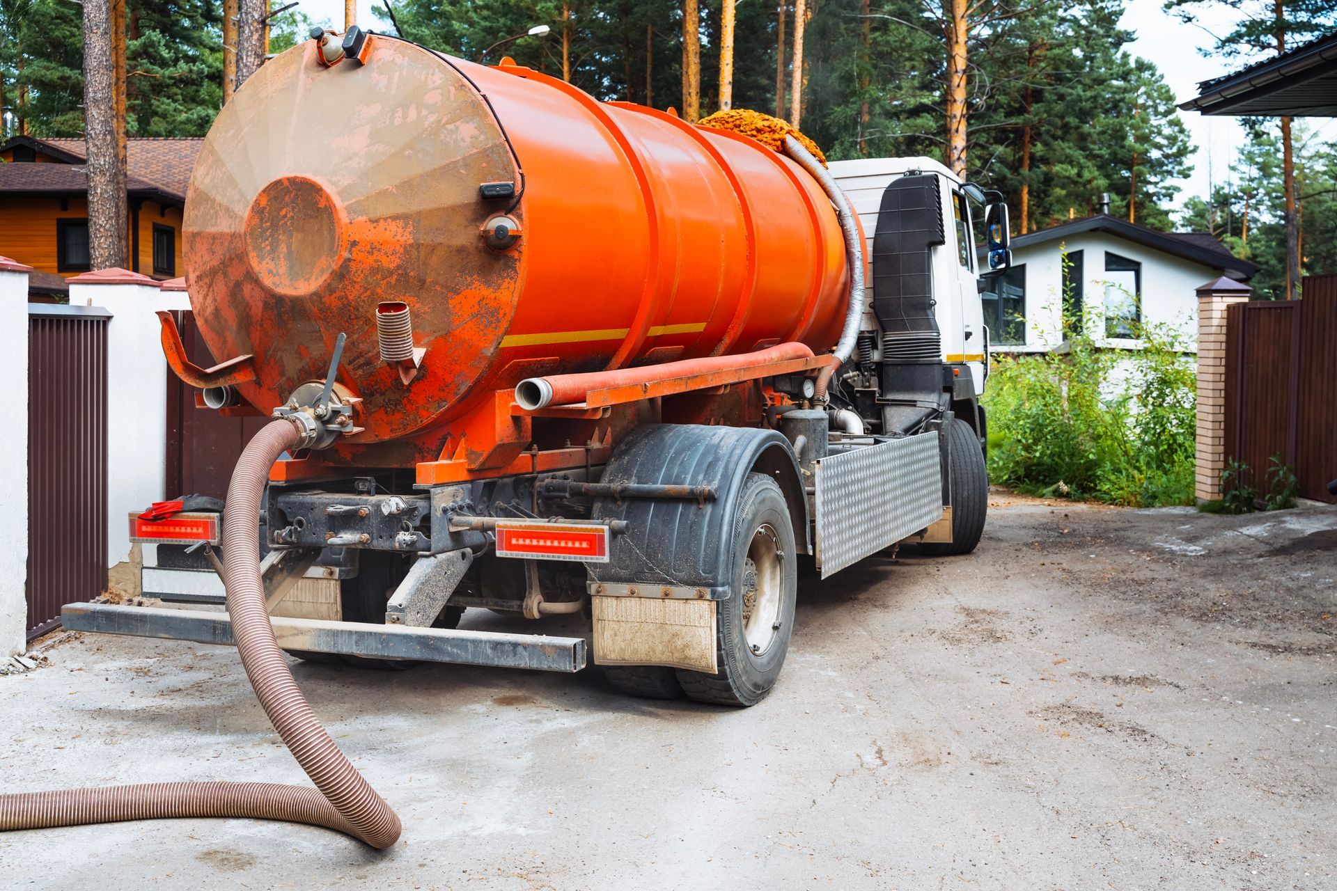 Orange septic truck parked in front of a house, hose extended.