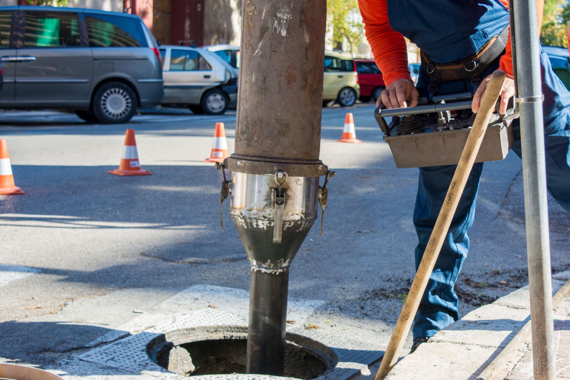 Utility worker near a manhole, using tools to access an underground pipe on a street.