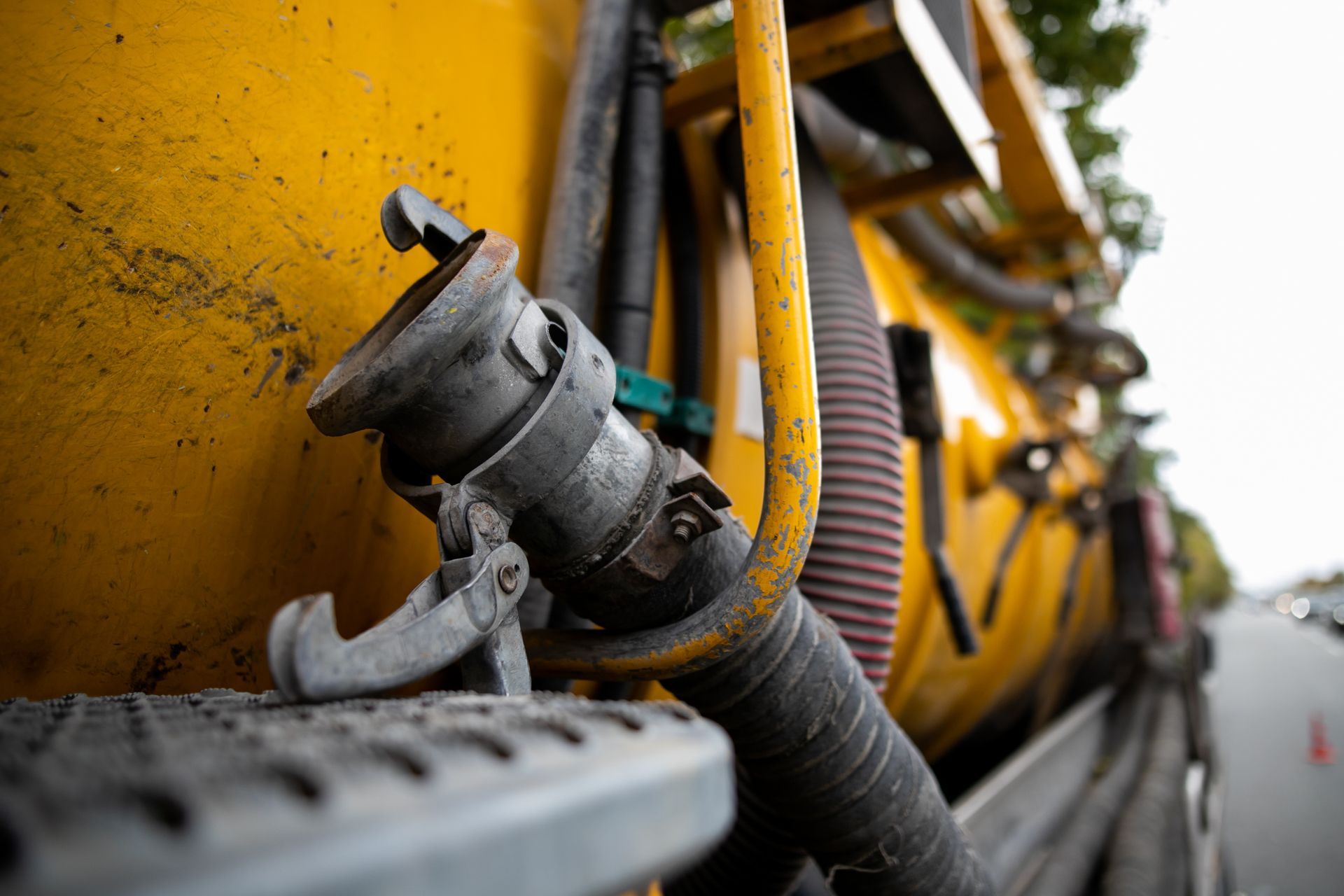 Yellow tanker truck's hose coupling with a metal handle, against a yellow tank, near a street.