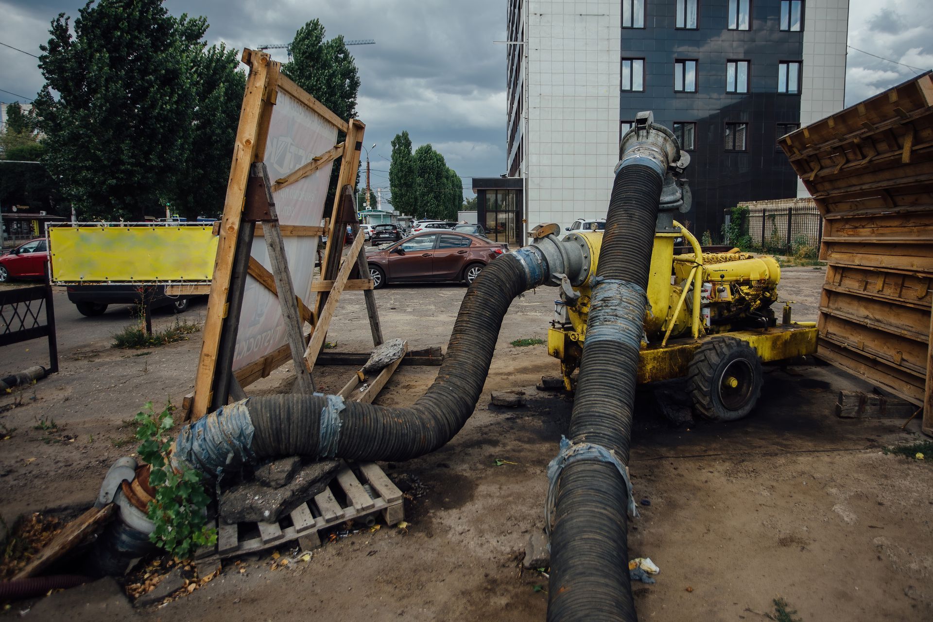 Yellow pump with large gray hoses on a city street. A building and parked cars are in the background.
