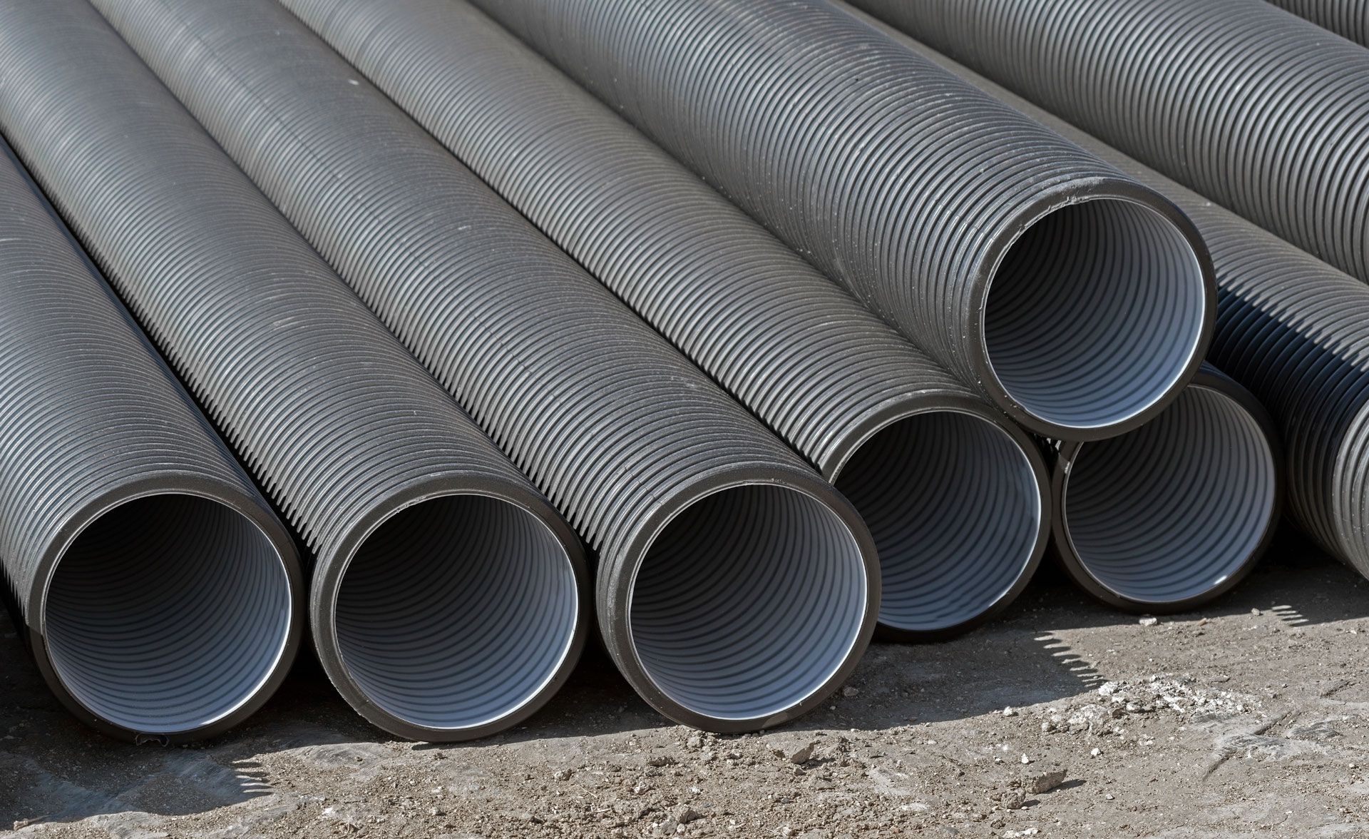 Several corrugated black plastic pipes stacked outdoors.