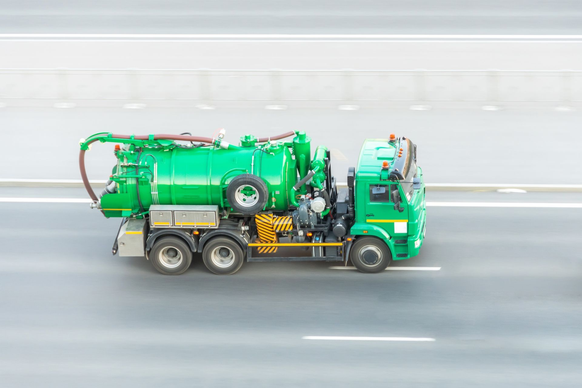Green vacuum truck driving on a highway.