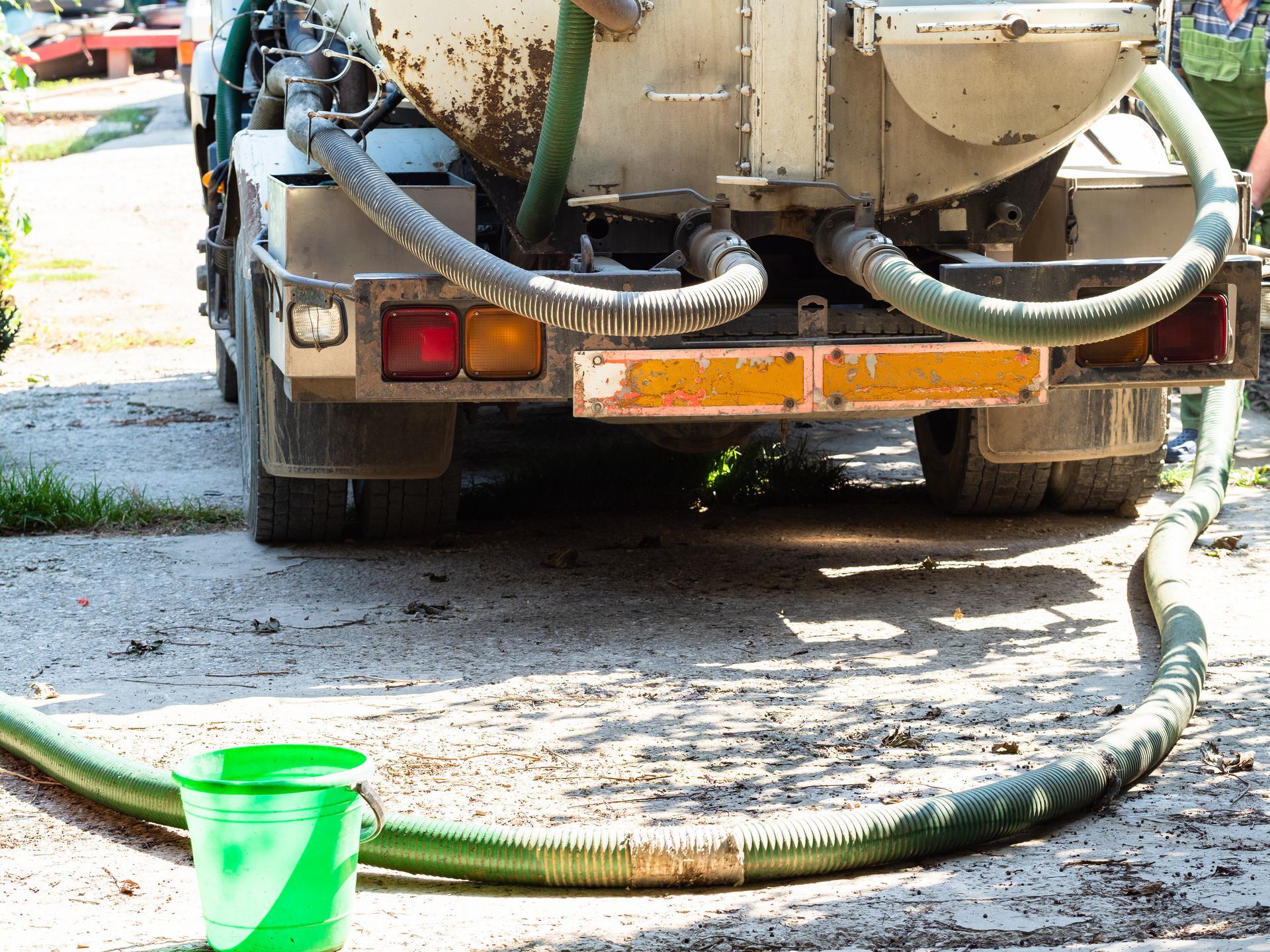 Rear of a sewage truck with a green hose, discharging into a green bucket.