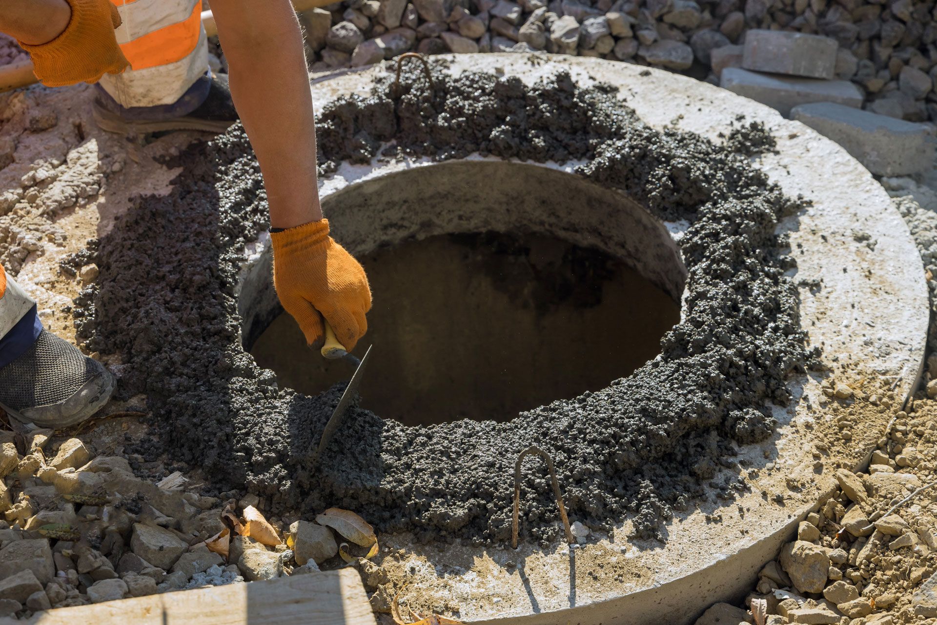 Construction worker using a trowel to apply mortar around a manhole cover.
