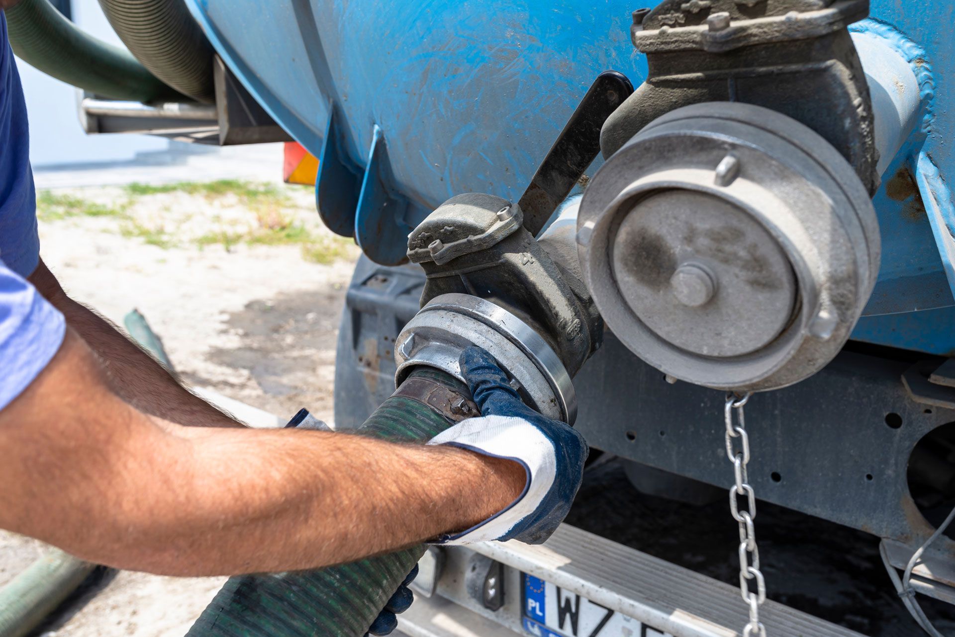 Person connecting a hose to a large blue tank on a truck, wearing gloves.