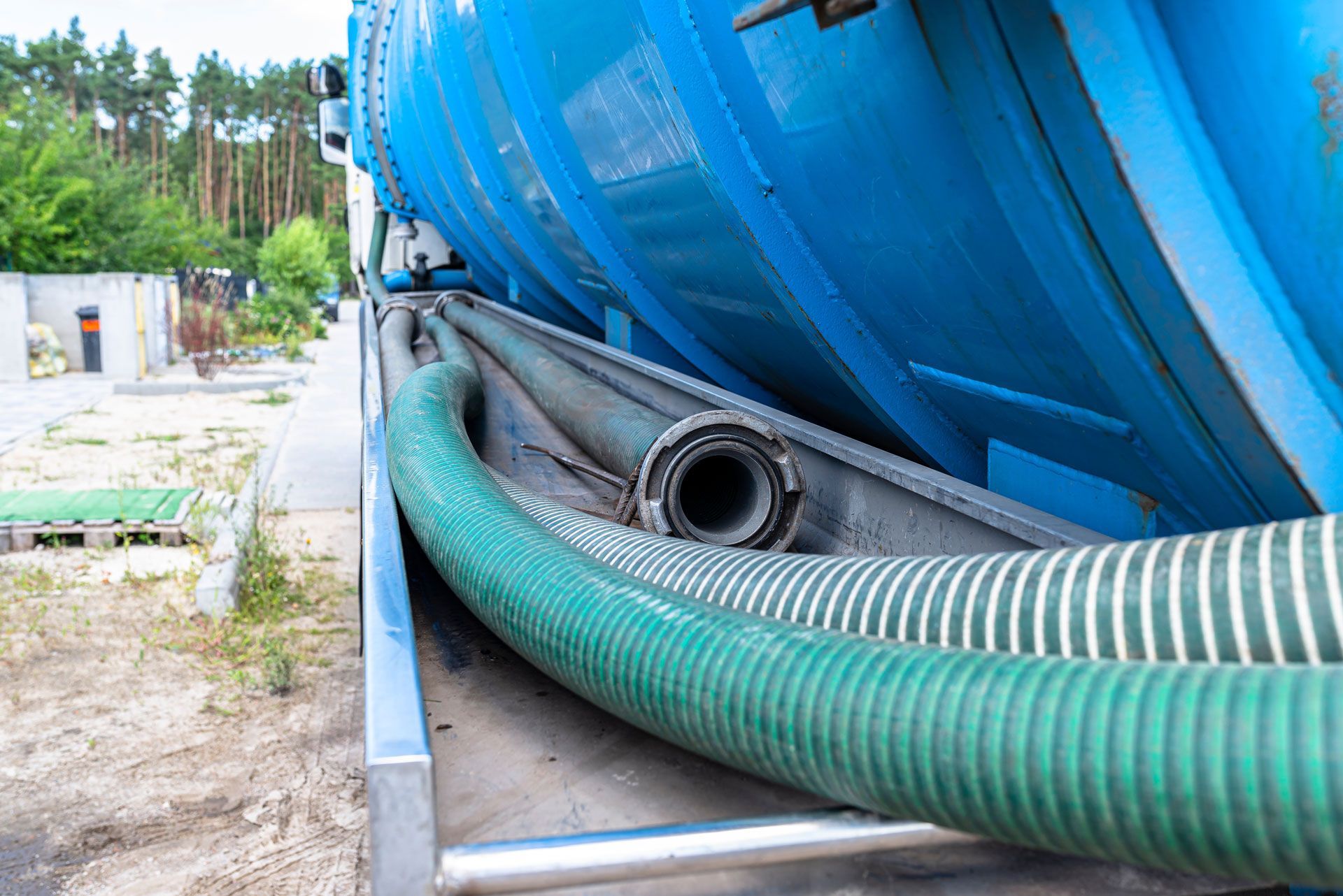 Blue tanker truck with green and white hoses alongside a road.
