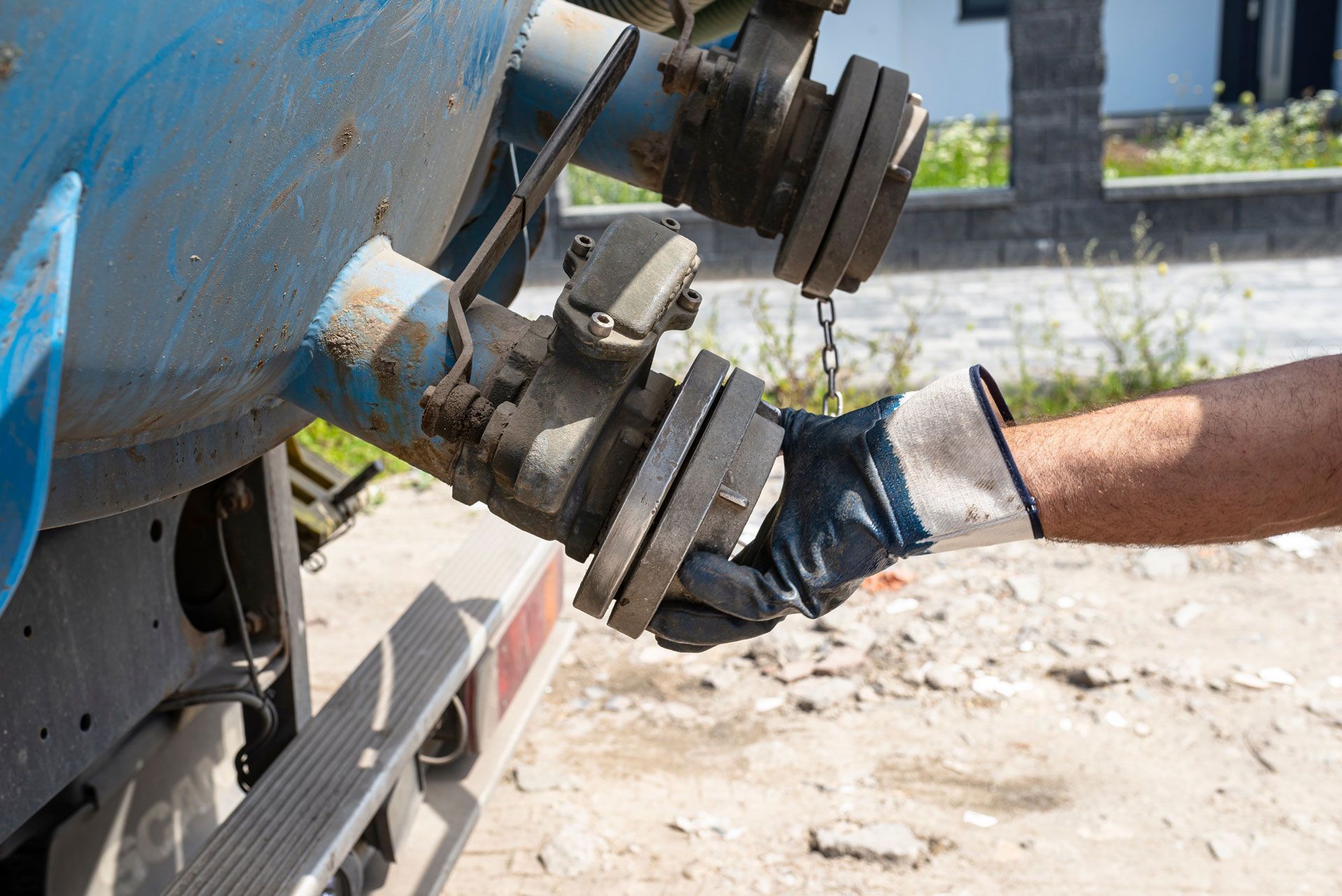 Hand in work glove holding a metal flange on blue tank, outdoor setting.