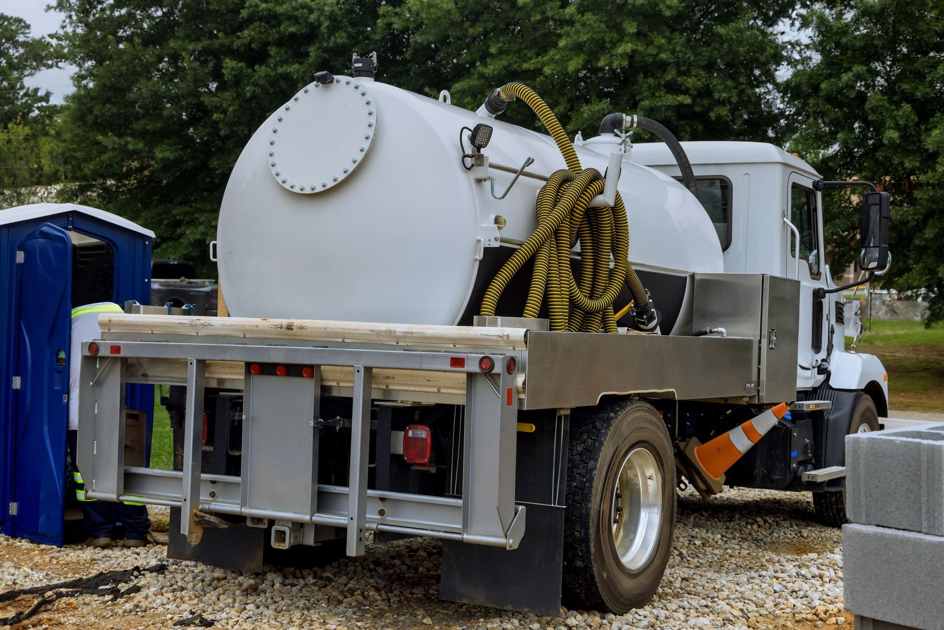 White septic tank truck at construction site next to blue portable toilet.
