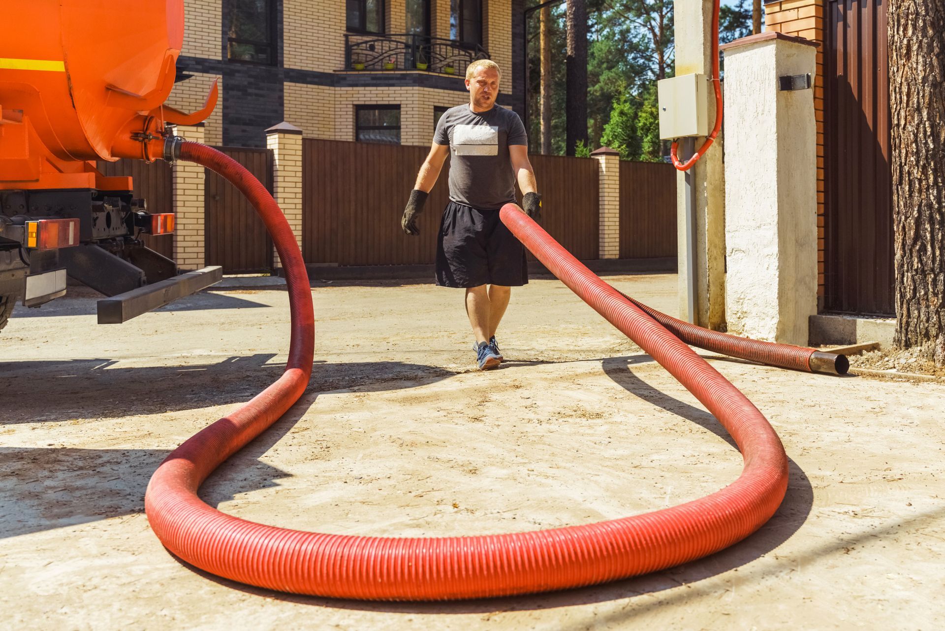 Man with hose connected to orange truck outside a house.