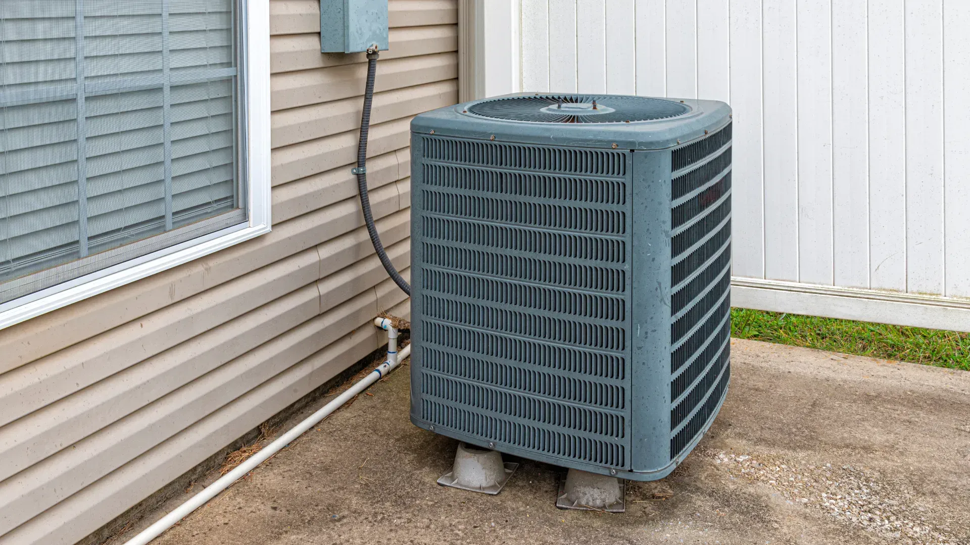 An air conditioner is sitting outside of a house next to a window.