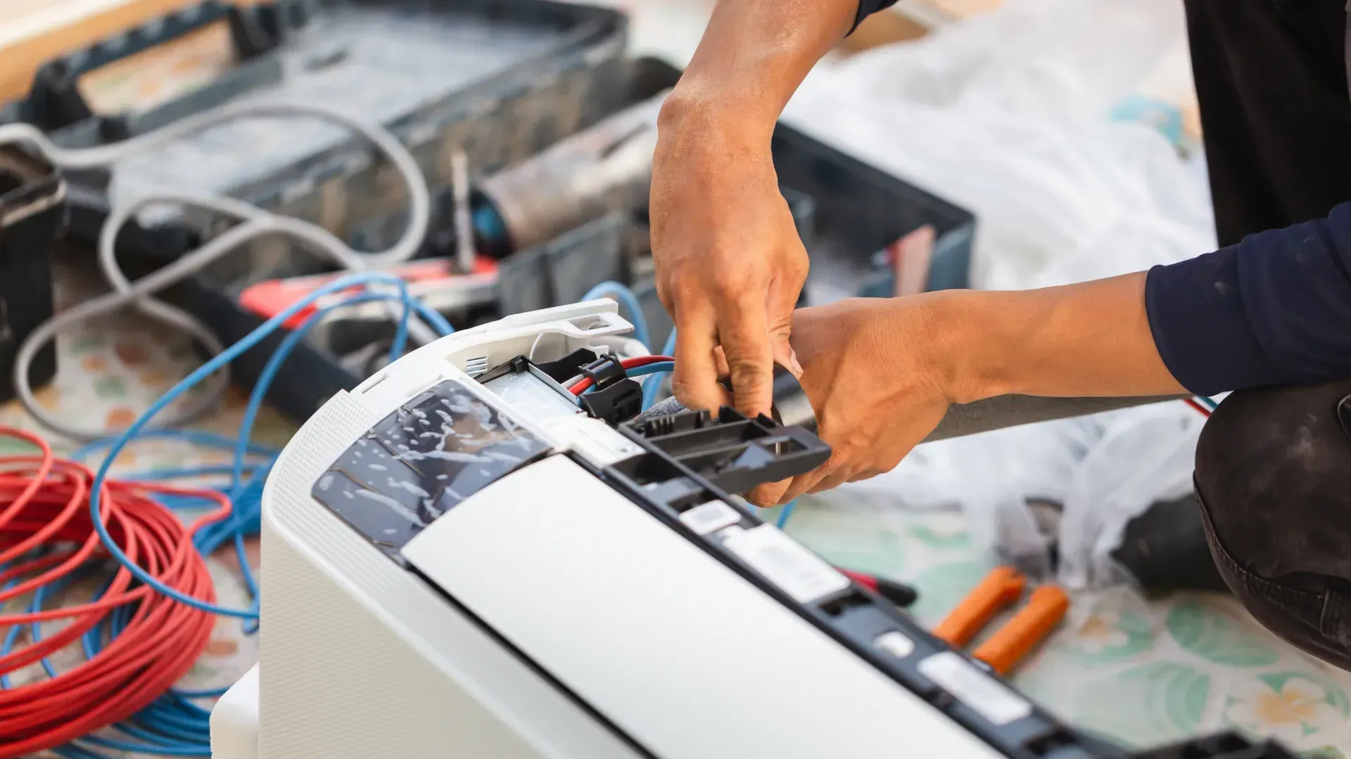 A man is sitting on the floor fixing an air conditioner.